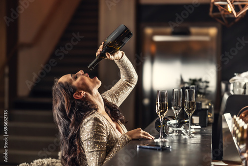 A tipsy woman drinks the last drops of champagne after New Years in the late morning at a bar photo