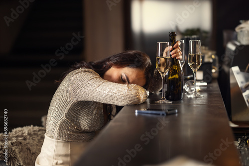 A drunk woman in a bar has fallen asleep on the bar counter, next to her is an empty champagne bottle and half-finished glasses photo