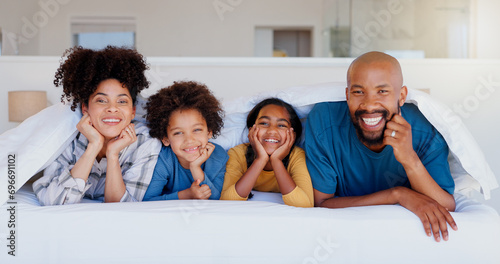 Happy, portrait and children with parents in bed of modern home for bonding together with love. Smile, fun and young interracial man and woman laying and relaxing with kids in bedroom of family house photo