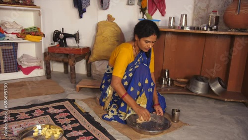 A middle-aged lower-class family lady is kneading the wheat dough for Chapatis / Rotis  small house  single room  migrant worker  dark skin. A rural Indian woman kneading the dough while adding wat...