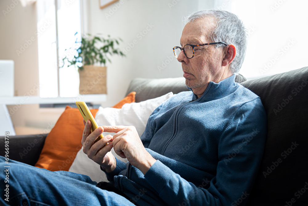 Senior caucasian man using mobile phone sitting on the sofa at home.