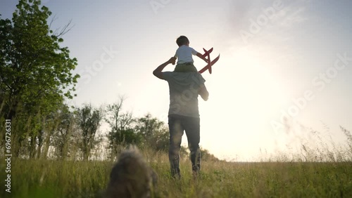 Wallpaper Mural Happy family on walk. Son sits on father's neck. Boy is playing with a toy plane. Family walk with dog. The kid sits on the shoulders of his father and plays with plane. Walk in nature on green grass Torontodigital.ca