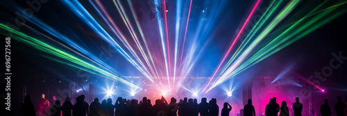 Rainbow-colored rays of laser beams are colorfully produced at concerts. The audience gets excited and cheers. Light for events and stages. Panorama for banner.