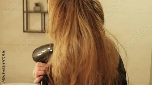 A woman with blonde hair using a hair dryer at home. Hair care.  photo