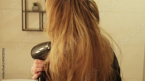 A woman with blonde hair using a hair dryer at home. Hair care. 