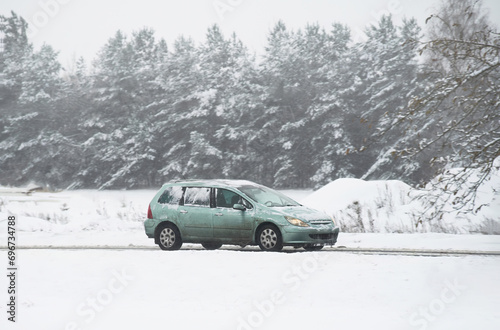 Winter road trip with a car. Car on a winter road with a lot of snow and ice. The car is equipped with winter tyres and is creating a splash of snow and water. Snowy landscape in the highway. © AlexGo