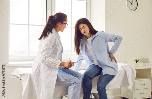 Pregnant woman feeling unwell suffering from backache during meeting with her gynecologist doctor in clinic. Female obstetrician consulting expectant girl sitting on the couch in office. photo