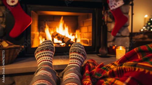 Feet in woolen socks next to the Christmas fireplace. Couple sitting under the blanket, she relaxes next to the warm fire.