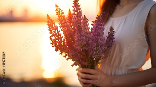 Close-up of a young woman with bare back and shoulders holding a bouquet of lupines in the sunset light,view behind.Simple slow living.Closeness to nature.Beauty concept.Selective focu : Generative AI