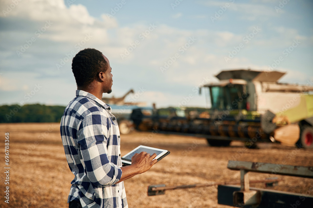 Standing, holding tablet. Beautiful African American man is in the agricultural field