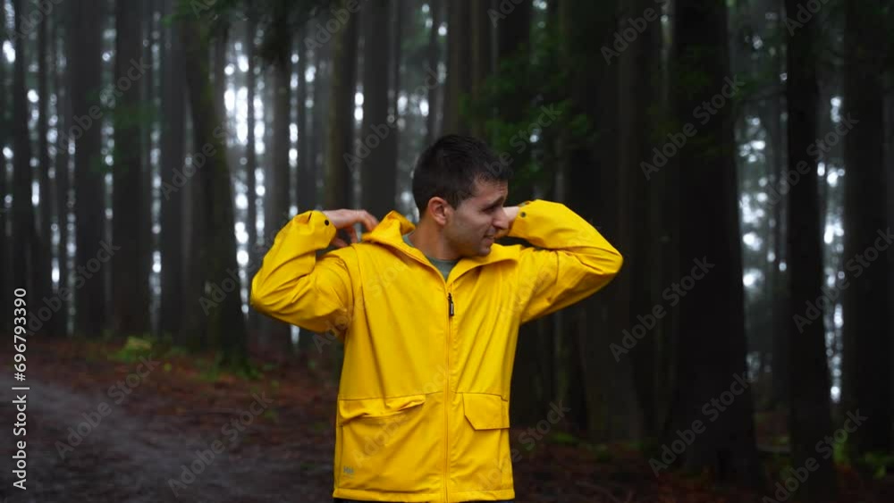 Man in the forest with a yellow raincoat covers his head from the rain