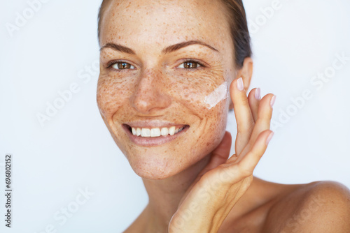 Beautiful woman with a freckles is applying a facial skincare cream and smiling. Beauty skin care,  hydration and moisturising treatment photo