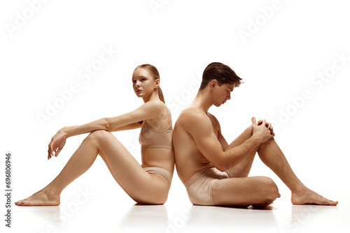 Couple, naked man and woman dressed in beige lingerie turned away and leaned on each other's backs against white background. Concept of beauty, love, body care, cosmetic products, fashion. Ad