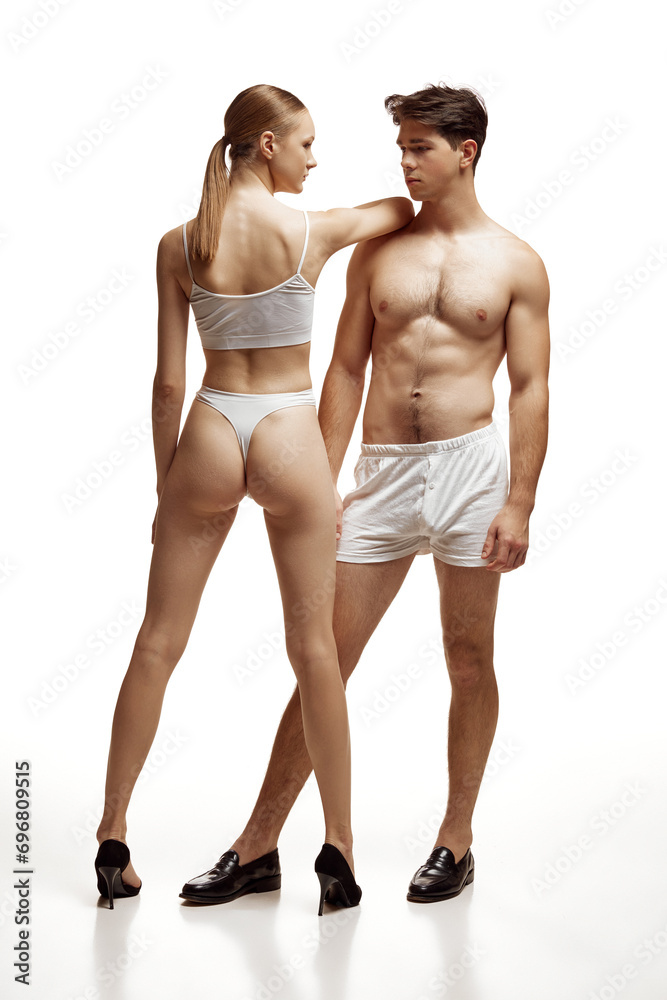 Full-length portrait of shirtless man and woman, elegantly posed in white underwear against pristine white studio background. Concept of natural beauty people, body care, cosmetic products, fashion.