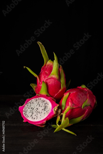 View of three pink pitayas or dragon fruits, one open, on table and black background, vertical, with copy space