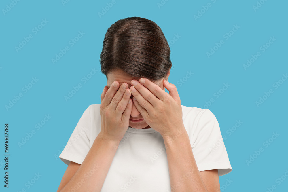 Resentful woman covering face with hands on light blue background Resentful woman covering face with hands on light blue background
