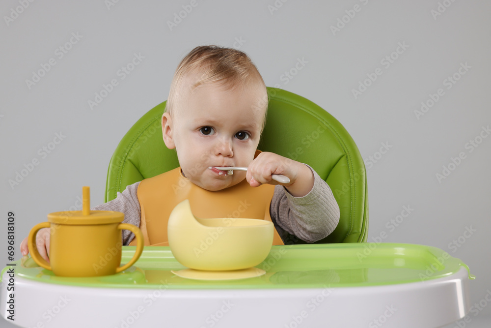 Cute little baby eating healthy food in high chair on gray background Cute little baby eating healthy food in high chair on gray background