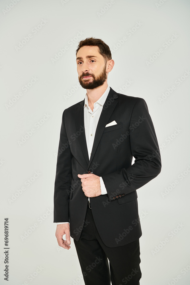 charismatic bearded businessman in black elegant suit looking away while standing on grey backdrop charismatic bearded businessman in black elegant suit looking away while standing on grey backdrop