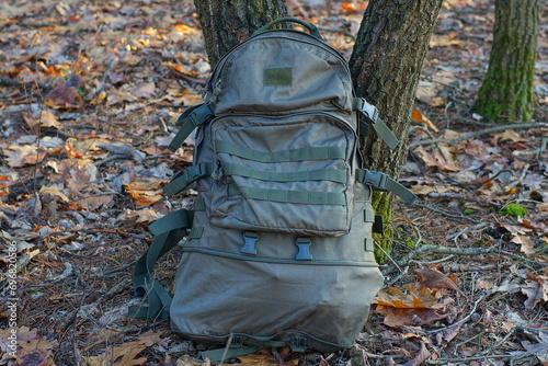 one olive color military man s closed with plastic zippers backpack stands on the ground near the trees during the day 