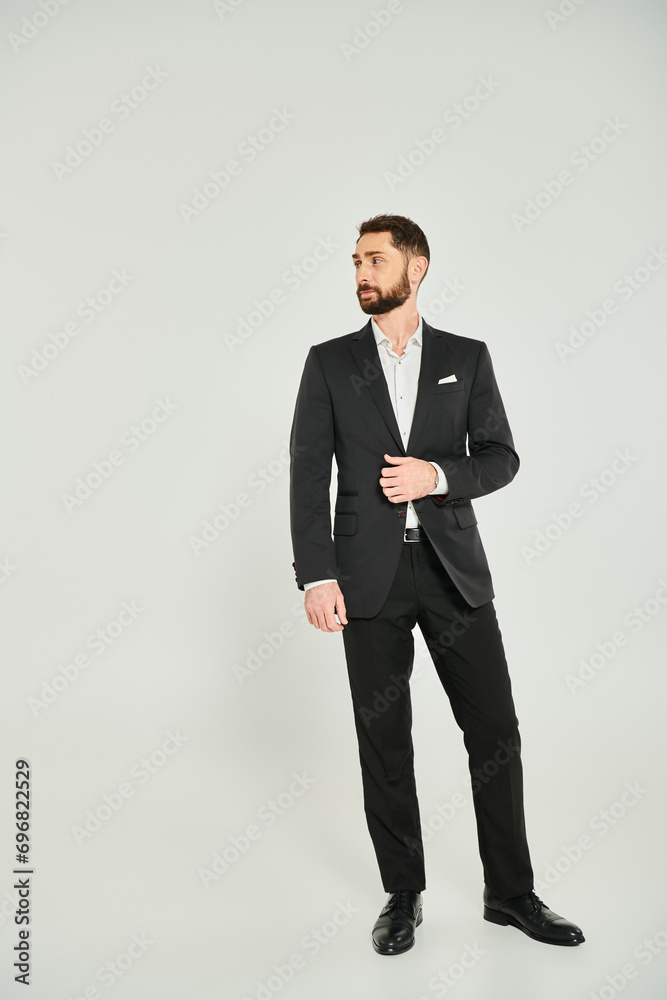 full length of stylish businessman in black elegant suit looking away while standing on grey full length of stylish businessman in black elegant suit looking away while standing on grey