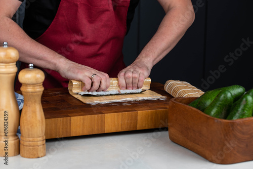 Sushi chef hands making Japanese food. Man cooking sushi at restaurant or at home. Traditional asian rolls on cutting board. Maki sushi with tuna, omelette, cheese and vegetables