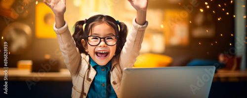 Asian Girl child in beige jacket with long hair sits at laptop in background of room at desk and raises her hand. School education. Online tutoring. Generation alpha. An ultra-wide banner. Copy space