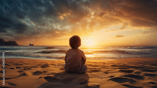 small boy or child sitting on beach contemplating the sea at sunset