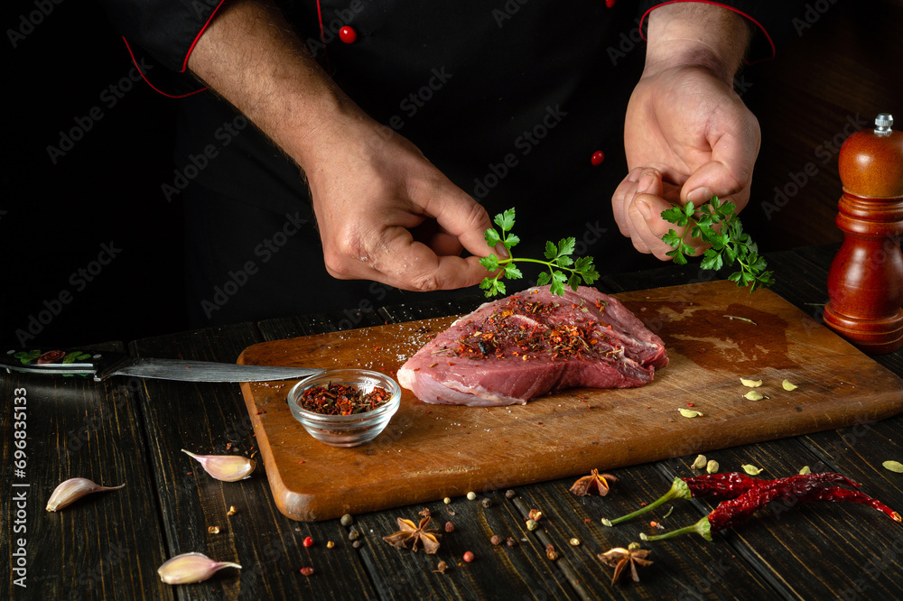 Adding parsley to meat by the chef hands for aroma and taste. Cooking veal steak on the kitchen table with spices and pepper