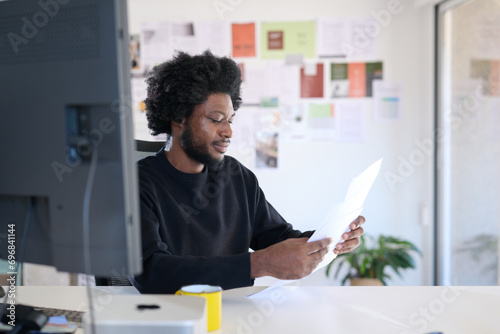 Focused Professional Reviewing Documents. concentrated professional man examines paperwork in a well-lit office, surrounded by colorful post-it notes and modern office equipment. photo