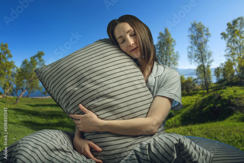 A young beautiful woman in pajamas with a pillow with her eyes closed in bed against the background of a lake and snowy mountains. A cozy, peaceful atmosphere of nature © Artem