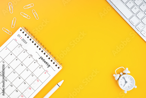 January 2024, Monthly desk calendar for 2024 year and alarm clock with paper clips on yellow color background.