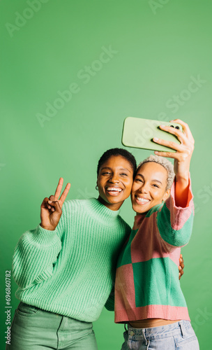 Foto Two young happy women taking a selfie in front of a green background in a studio
