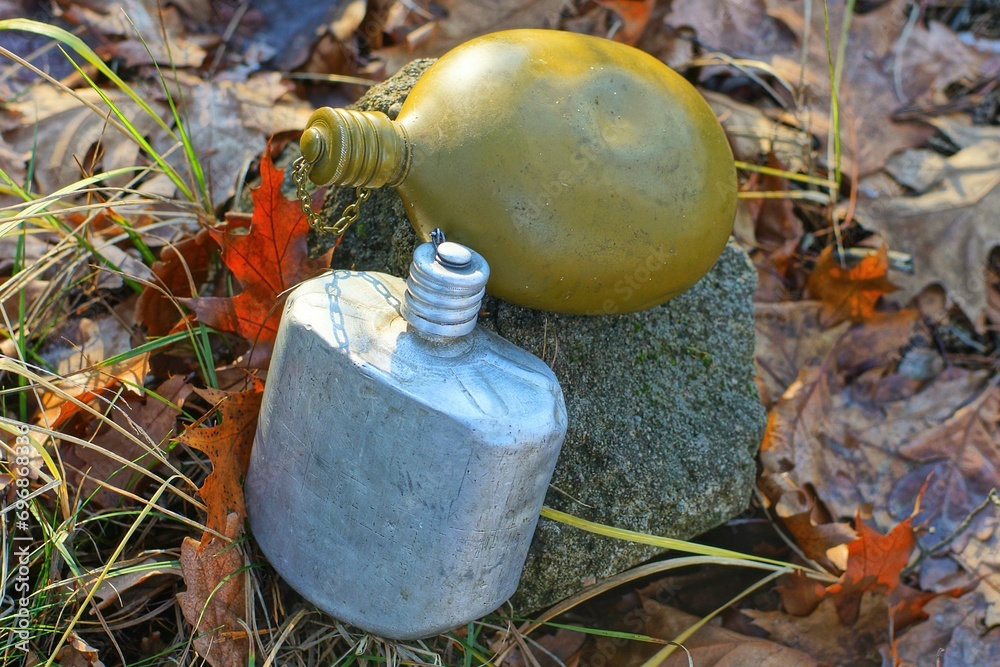 Obraz premium two different empty dirty old manual aluminum gray and olive army closed flasks lie on the ground near a gray stone on the street 