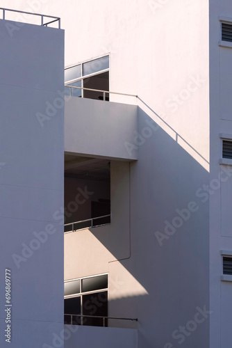 The connective corridor between white modern office buildings with light and shadow on surface in vertical frame  minimal exterior architecture background in street photography style concept