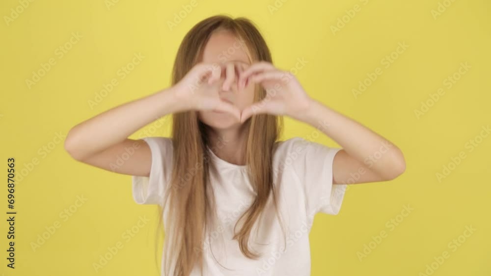 little girl kid demonstrates heart sign with hands, isolated on yellow color background wall in studio. little girl kid demonstrates heart sign with hands, isolated on yellow color background wall in studio.