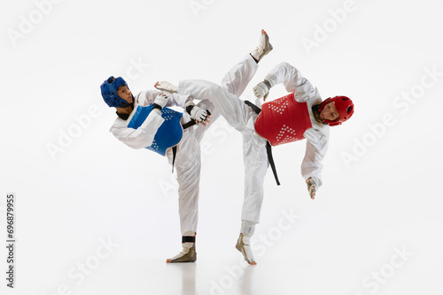 Dynamic image of young men, taekwondo athletes in kimono and helmets training isolated over white background. Concept of martial arts, combat sport, competition, action, strength, education photo