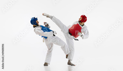 Two men in kimono and helmets practicing taekwondo, training, fighting isolated over white background. Concept of martial arts, combat sport, competition, action, strength, education photo