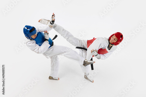Competitive young men, taekwondo athletes fighting, hitting with legs isolated over white background. Concept of martial arts, combat sport, competition, action, strength, education