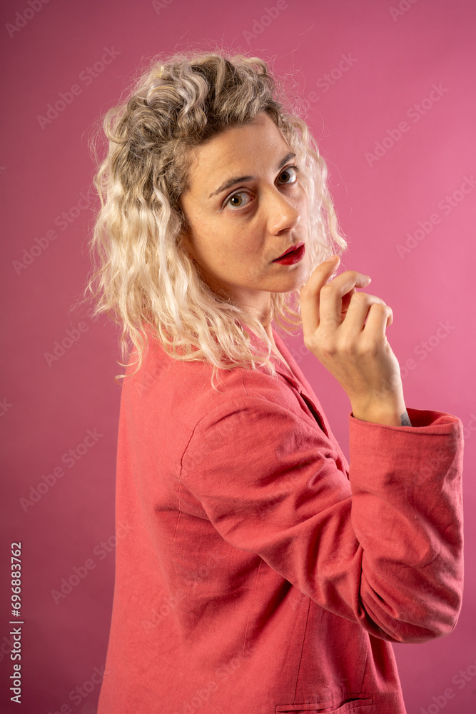 Portrait of a happy young woman in a pink jacket isolated on a pink background leaning on a high chair with a tiara on her head wearing a dress