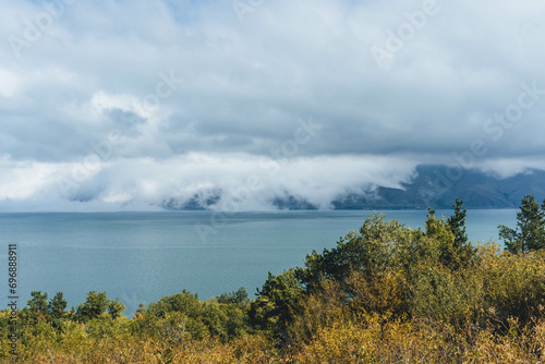 amazing beautiful top view of blue sevan lake in armenia with autumn trees below and vegetation with fluffy white clouds around photo