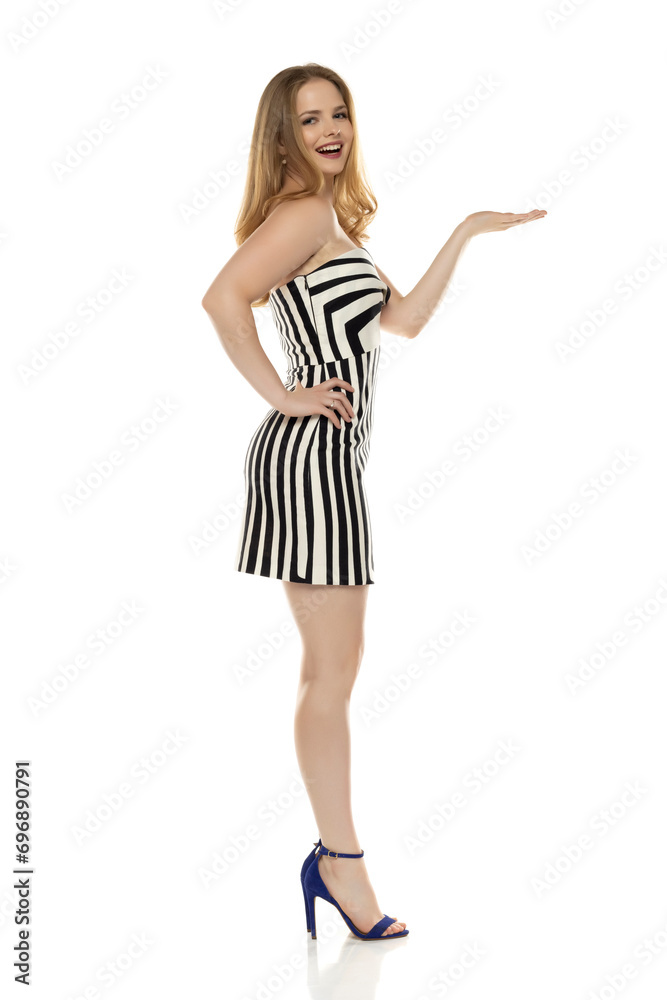 Full body side view portrait of elegant lovely blond lady  holding imaginary product on her palm on white background in black and white short summer dress