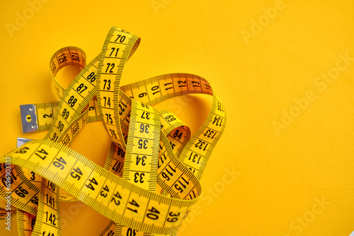 Yellow measuring tape on a yellow background. Tool for measuring length and volume. Tape for measuring in the clothing industry or the volume of the human body
 photo