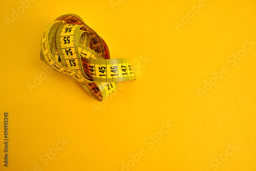 Yellow measuring tape on a yellow background. Tool for measuring length and volume. Tape for measuring in the clothing industry or the volume of the human body