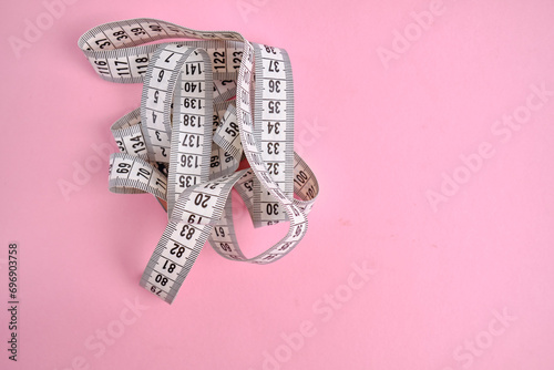White measuring tape on a rose background. Tool for measuring length and volume. Tape for measuring in the clothing industry or the volume of the human body 