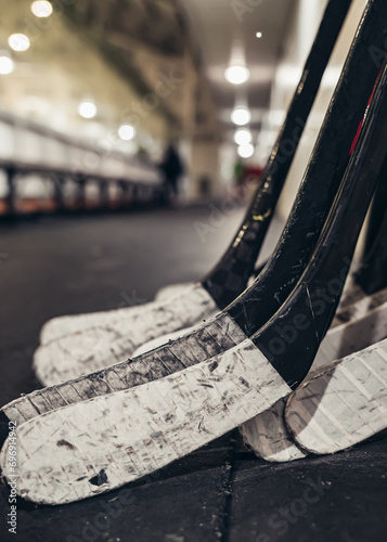 Worn taped ice hockey sticks leaning on the wall at a hockey arena with a blurred background 
