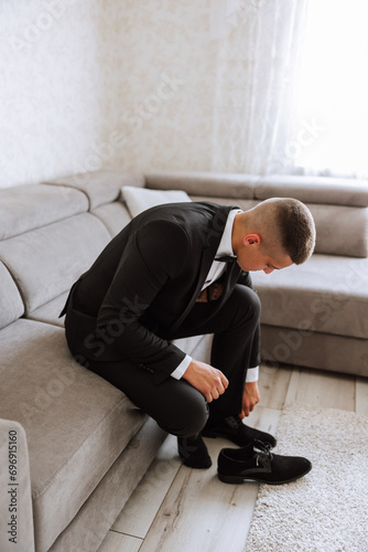 A man's hands tie the laces of his new shoes. People, business, fashion and footwear concept - close-up of a man's legs and hands tying shoelaces. The groom puts on his shoes. © Vasil