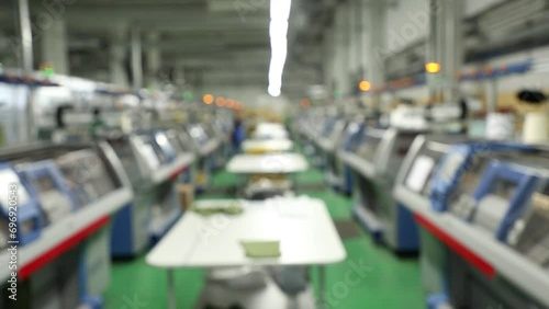 Blurred background view of working knitting machine in workshop. A row of industrial textil flat knitting machines in a knitwear factory. Manufacture of knitwear, modern computerized flat Knitting