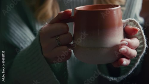 Close up of woman wearing cosy jumper sitting on sofa at home drinking hot coffee from cup - shot in slow motion photo