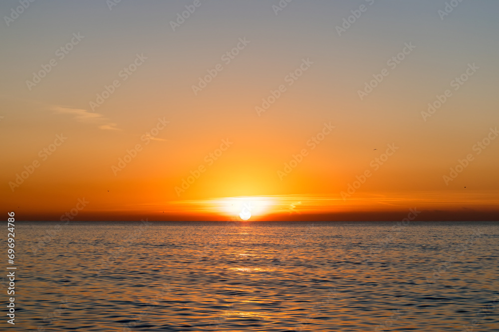 Bright sunset with a big yellow sun above the sea surface.