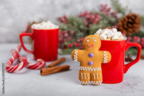 Hot drink with marshmallows and candy cane in a red cup on a texture table.Cozy seasonal holidays.Hot cocoa with gingerbread Christmas cookies.Hot chocolate with marshmallow and spices.Copy space.